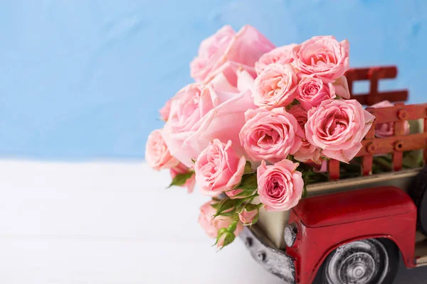 Retro car with pink roses flowers against blue wall. Romantic background. Selective focus. Place for text.