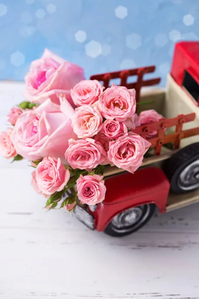 Retro car with pink roses flowers against blue wall. Romantic background. Selective focus. Vertical image.