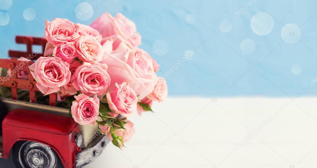 Retro car with pink roses flowers against blue wall. Romantic background. Selective focus. Place for text. 