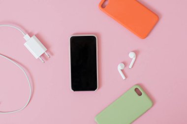 Kulaklıklı, şarjlı ve pembe arka planda renkli silikon çantalı bir akıllı telefonun üst görüntüsü.