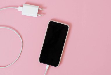 Moda pembe arka planda şarjı olan bir akıllı telefonun üst görünümü.