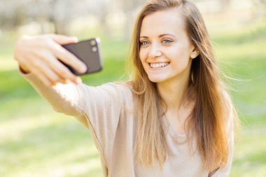 Dışarıda selfie çeken gülümseyen genç bir kadının portresi..