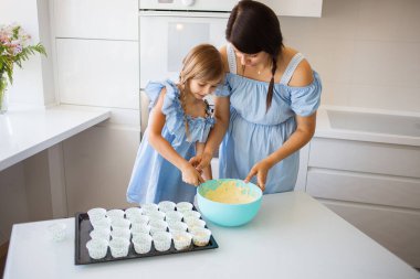 Mutlu anne ve kız yemek pişiriyor ve birlikte beyaz mutfakta eğleniyorlar..
