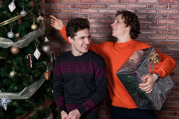 Два веселых молодых человека празднуют Рождество за кирпичной стеной — стоковое фото