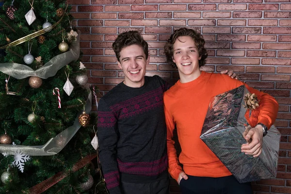 Два веселых молодых человека празднуют Рождество за кирпичной стеной — стоковое фото