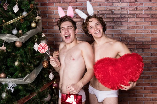Двоє смішних хлопців у костюмах кроликів святкують Різдво над цегляною стіною — стокове фото