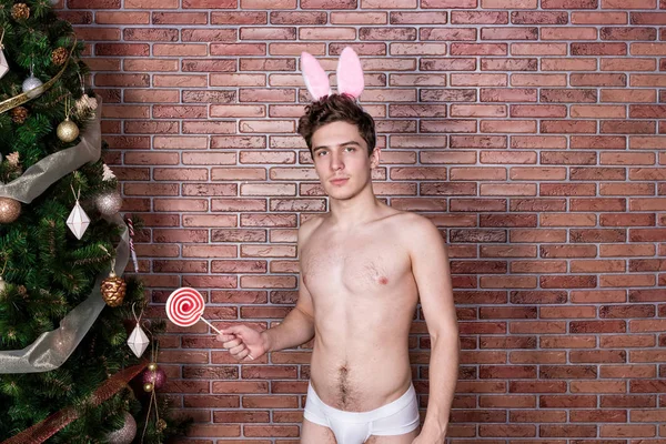 Fešák nahý chlap v obleku králík slaví Vánoce přes cihlovou zeď — Stock fotografie