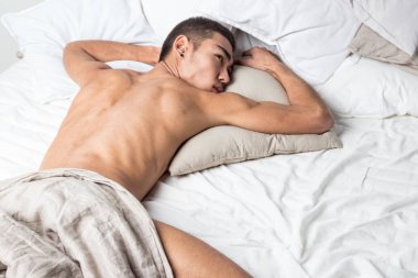 Genç yakışıklı adam yatakta dinleniyor. Seksi çıplak adam dinleniyor.
