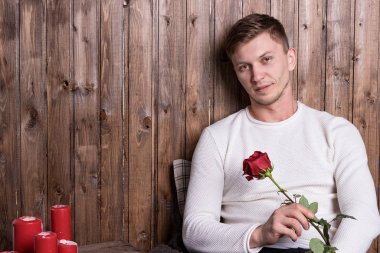 Ellerinde gülle tahta duvarın yanında oturan yakışıklı genç adam.