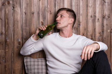 Genç yakışıklı adam ahşap duvarın yanında oturuyor ve bira içiyor.
