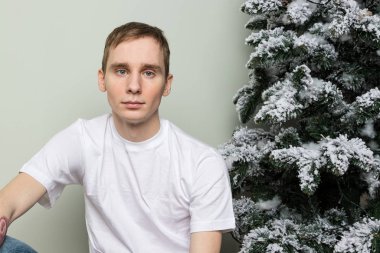 Büyük hediyeli genç adam Noel ağacının yanında yerde oturuyor.