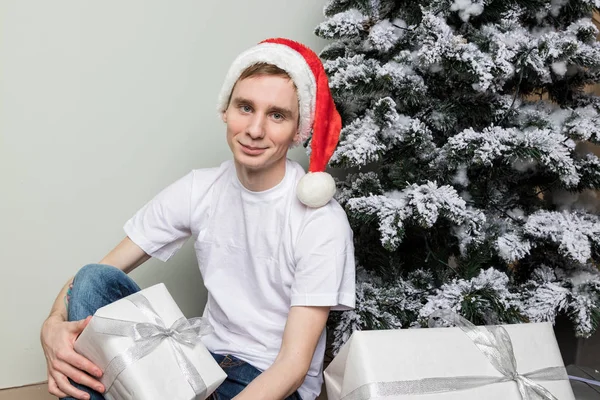 Mladý muž s velkým dárkem sedí na podlaze v blízkosti vánoční strom — Stock fotografie