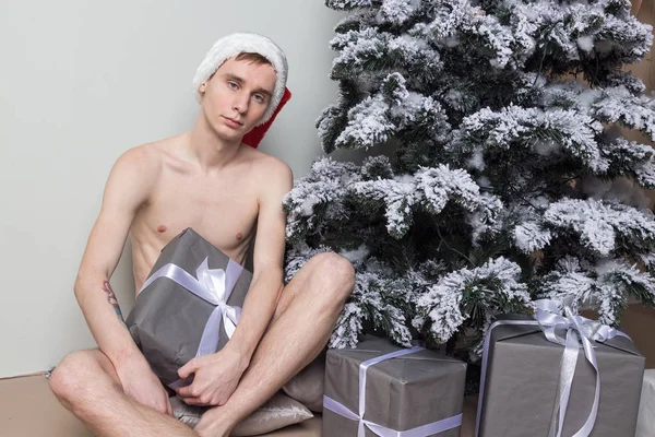 Mladý muž s velkým dárkem sedí na podlaze v blízkosti vánoční strom — Stock fotografie