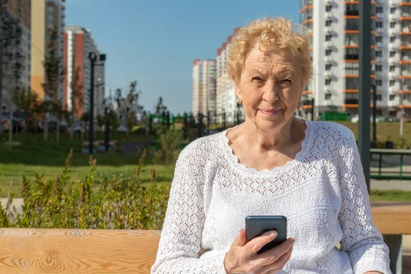 Relaxed elder woman sitting on a bench looking at camera and smiling