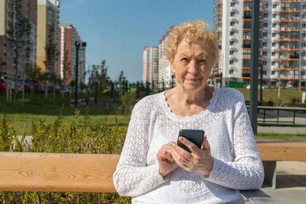 Relaxed elder woman sitting on a bench looking at camera and smiling