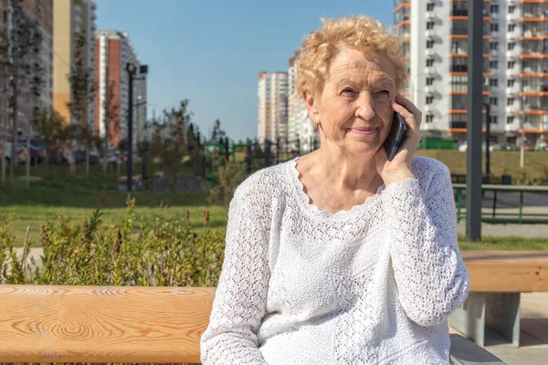 Relaxed elder woman sitting on a bench looking at camera and smiling