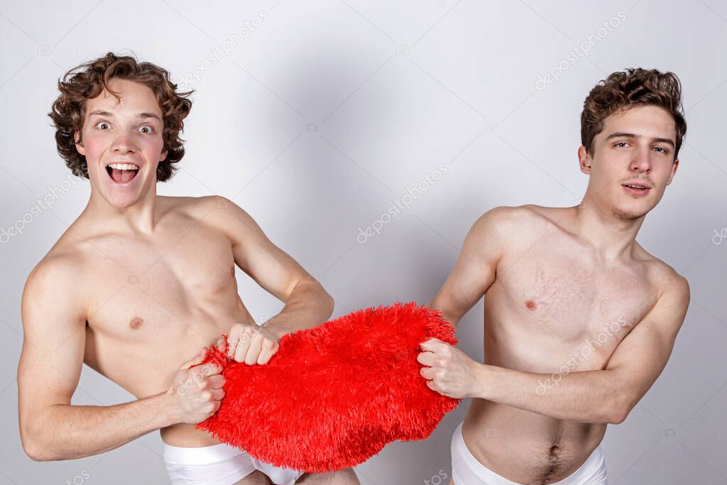 Two naked guys pull a big red heart in different directions on white background
