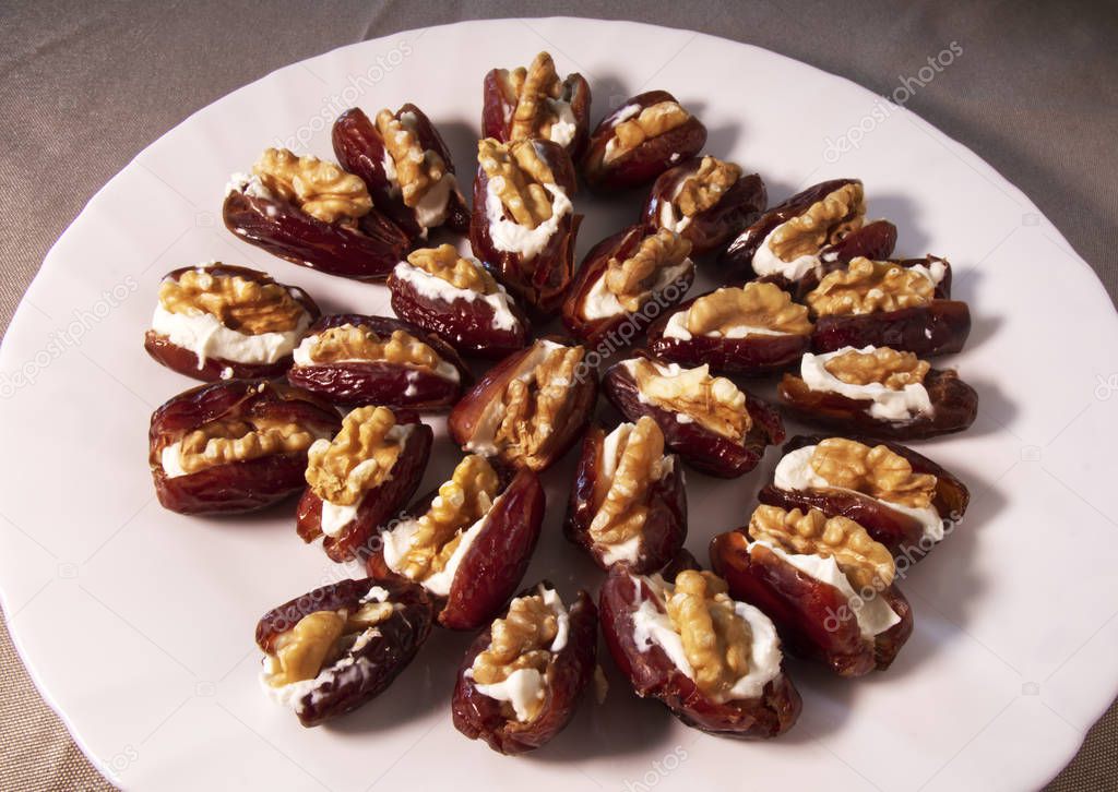 Fresh dates filled with mascarpone cheese and walnuts in a white dish.