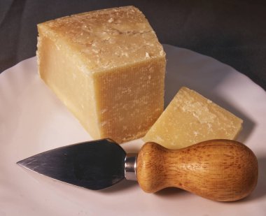 Beyaz bir tabakta peynir bıçağıyla İtalyan parmesan reggiano peyniri dilimi..