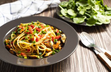 Geleneksel İtalyan deniz ürünleri spagettisi midyeli ve salatalı ahşap bir masada servis ediliyor..