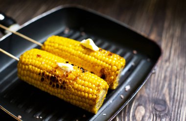 Köhne ahşap arka planda ızgara tavada tereyağı ve tuzlu leziz ızgara mısır. Yakın çekim.