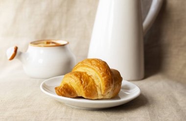 Beyaz ahşap masada kahve ve fincanlı taze kruvasan.