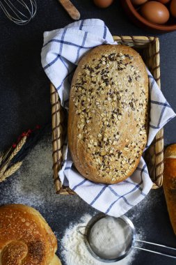 Pastane kavramı. Koyu arkaplandaki farklı ekmek çeşitleri. Sepette ekmek, yumurta, un, buğday kulağı.
