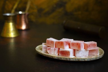 Eski bir tabakta gül suyu aromalı Türk Lokum (Loukoumi, Ratluk). Arka planda iki bakır antika çerez ve bir kahve öğütücü var. Altın arka plan. Ön manzara. Boşluğu kopyala