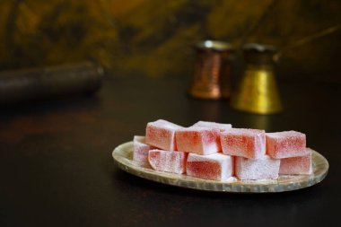 Eski bir tabakta gül suyu aromalı Türk Lokum (Loukoumi, Ratluk). Arka planda iki bakır antika çerez ve bir kahve öğütücü var. Altın arka plan. Ön manzara. Boşluğu kopyala