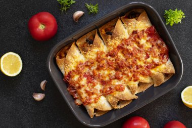 Tavuk, sebze, mısır, fasulye, domates sosu ve peynirli Meksika enchilada 'sı. Fırın tepsisinde servis edilmiş. Meksika yemeği. Latin Amerika mutfağı. Siyah arkaplan, üst görünüm, kopyalama alanı