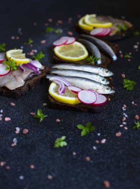 Smorrebrod, geleneksel İskandinav açık sandviçleri koyu çavdar ekmeği, ringa balığı, ançüez, turp, soğan ve hardal soslu. Siyah arka plan. Yakın çekim, seçici odaklanma.