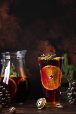 Sıcak şarap. Kırmızı şaraptan, turunçlardan ve baharatlardan yapılmış sıcak bir içecek. Tahta bir masada Noel süsleriyle. Bardak ve sürahi ile sıcak şarap. Karanlık arka plan. Yakın plan, renkli, kopyalama alanı