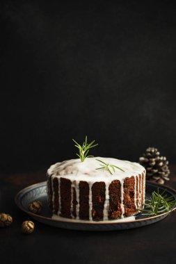 Geleneksel Noel pastası, üzerinde meyve ve fındık olan koyu masa ve siyah arka plan. Kış tatili için tatlı. Noel süslemeleri ve ışıklar. Boşluğu kopyala