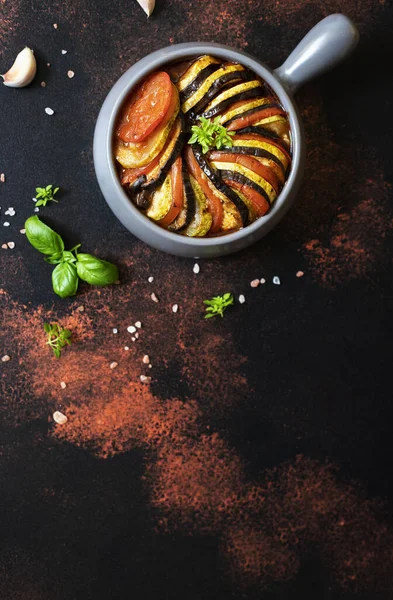 Ratatouille traditional french dish of baked summer vegetables served in a baking tray. Vegetarian and diet food. French cuisine/food. Dark rustic background, top view, copy space