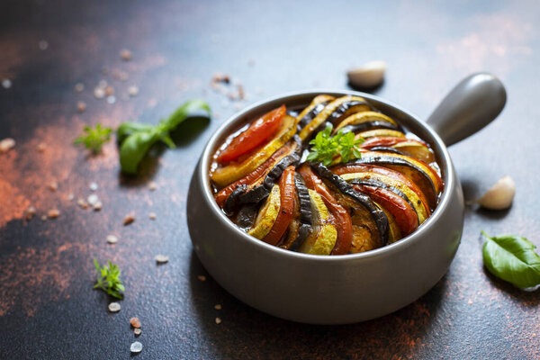Ratatouille traditional french dish of baked summer vegetables served in a baking tray. Vegetarian and diet food. French cuisine/food. Dark rustic background, top view, copy space
