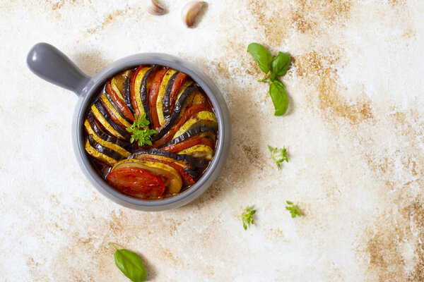 Ratatouille traditional french dish of baked summer vegetables served in a baking tray. Vegetarian and diet food. French cuisine/food. Marble light background, top view, copy space