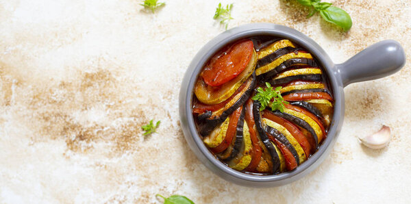 Ratatouille traditional french dish of baked summer vegetables served in a baking tray. Vegetarian and diet food. French cuisine/food. Marble light background, top view, copy space