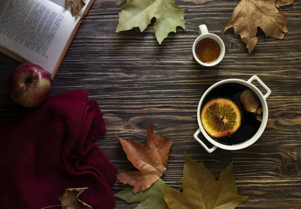 Warm autumn and winter alcoholic drink mulled wine. Honey, autumn leaves, apples, a book and a woolen sweater on a wooden background. Autumn cozy mood. Autumn background. Flat lay