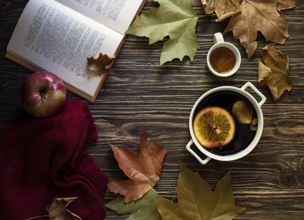 Warm autumn and winter alcoholic drink mulled wine. Honey, autumn leaves, apples, a book and a woolen sweater on a wooden background. Autumn cozy mood. Autumn background. Flat lay