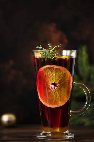 Mulled wine a warm drink made of red wine, citruses and spices on a wooden table with Christmas decorations. Glass and decanter with mulled wine. Dark background. Closeup, colorful, copy space