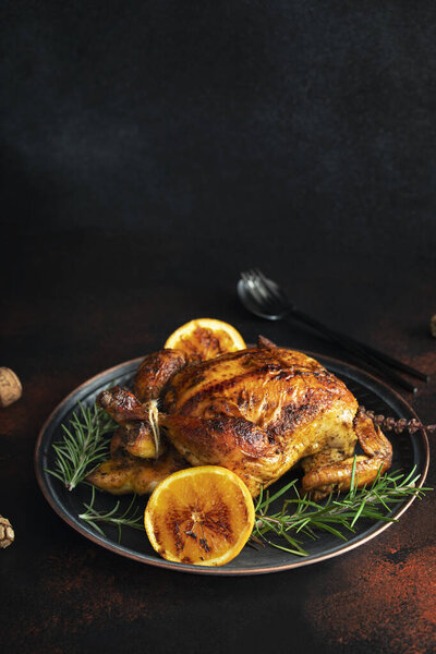 Roasted whole chicken for Christmas or New Year on a dark background with Christmas decorations. Baked Chicken with Oranges and rosemary. Christmas dinner. Space for text. Selective focus