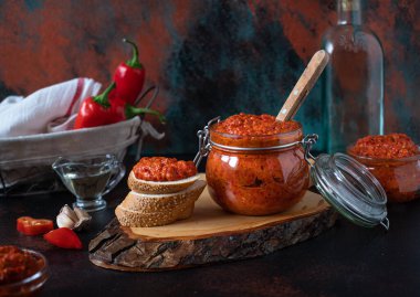Geleneksel Balkan aperatifi ya da ahşap kesme tahtasındaki cam kavanozlarda servis edilen kavrulmuş kırmızı biber sosu. Ekmek, kırmızı biber, yağlı bir şişe, kırmızı biber tozu. Kırsal koyu arkaplan