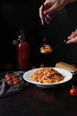 Domates soslu ve parmesanlı makarna. Arka planda makarna olan beyaz tabak. Çatal tutan kadın eller ve spagettili kaşık. Çatallı spagetti. Alçak tuş, dikey, kopyalama alanı