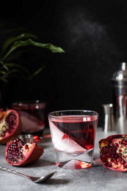 Gri masa ve siyah arka planda nar içeceği. Dilimlenmiş nar, kokteyl karıştırıcı ve bar aletleri. Nar kokteyli. Nar suyunu buzla tazeliyorum.