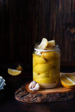 Koyu bir masa ve arka planda cam bir kavanozda fermente edilmiş limonlar. Konserve tuzlu limon. Probiyotikler ve mayalanmış yiyecekler. Kopyalama uzayı. Yakın plan.