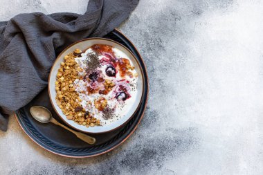 Fındıklı granola, Yunan yoğurdu, organik reçel ve chia tohumları beyaz bir kase ve bakır tepside servis edilir. Sağlıklı kahvaltı, sağlıklı beslenme konsepti. Gri arkaplan, üst görünüm, kopyalama alanı