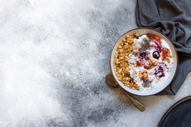 Fındıklı granola, Yunan yoğurdu, organik reçel ve chia tohumları beyaz bir kase ve bakır tepside servis edilir. Sağlıklı kahvaltı, sağlıklı beslenme konsepti. Gri arkaplan, üst görünüm, kopyalama alanı