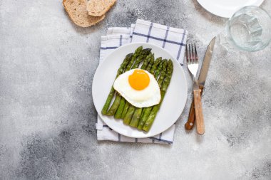 Beyaz tabakta servis edilen organik sağlıklı kuşkonmaz ve kızarmış yumurta. Sağlıklı vejetaryen kahvaltısı. Gri arka plan. Uzayı kopyala Düz yatıyordu