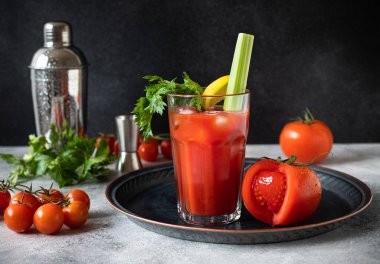 Classic alcoholic cocktail Bloody Mary with ice, lemon and celery. Cocktail ingredients and bar tools on a gray table and black background clipart