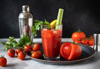 Klasik alkollü Bloody Mary kokteyli. Buzlu, limonlu ve kerevizli. Gri masa ve siyah arkaplan üzerinde kokteyl malzemeleri ve bar araçları